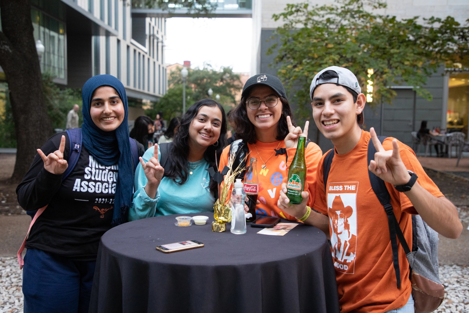 Four students standing around a table showing hookem signs with their hands and smiling